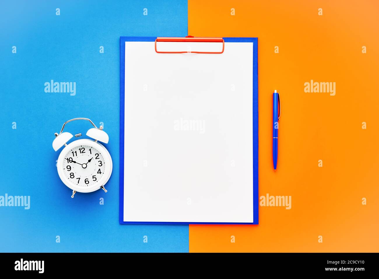 Leeres Clipboard-Modell, ein blauer Stift und ein weißer Wecker auf dem blau-orangefarbenen Hintergrund. Draufsicht, Kopierbereich für Text. Zurück in die Schule, Deadline Stockfoto