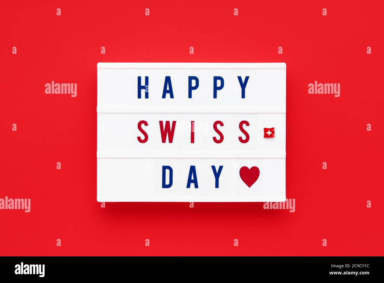 HAPPY SWISS DAY in einem Leuchtkasten auf rotem Hintergrund geschrieben. Datum des Unabhängigkeitstages. Draufsicht. Stockfoto