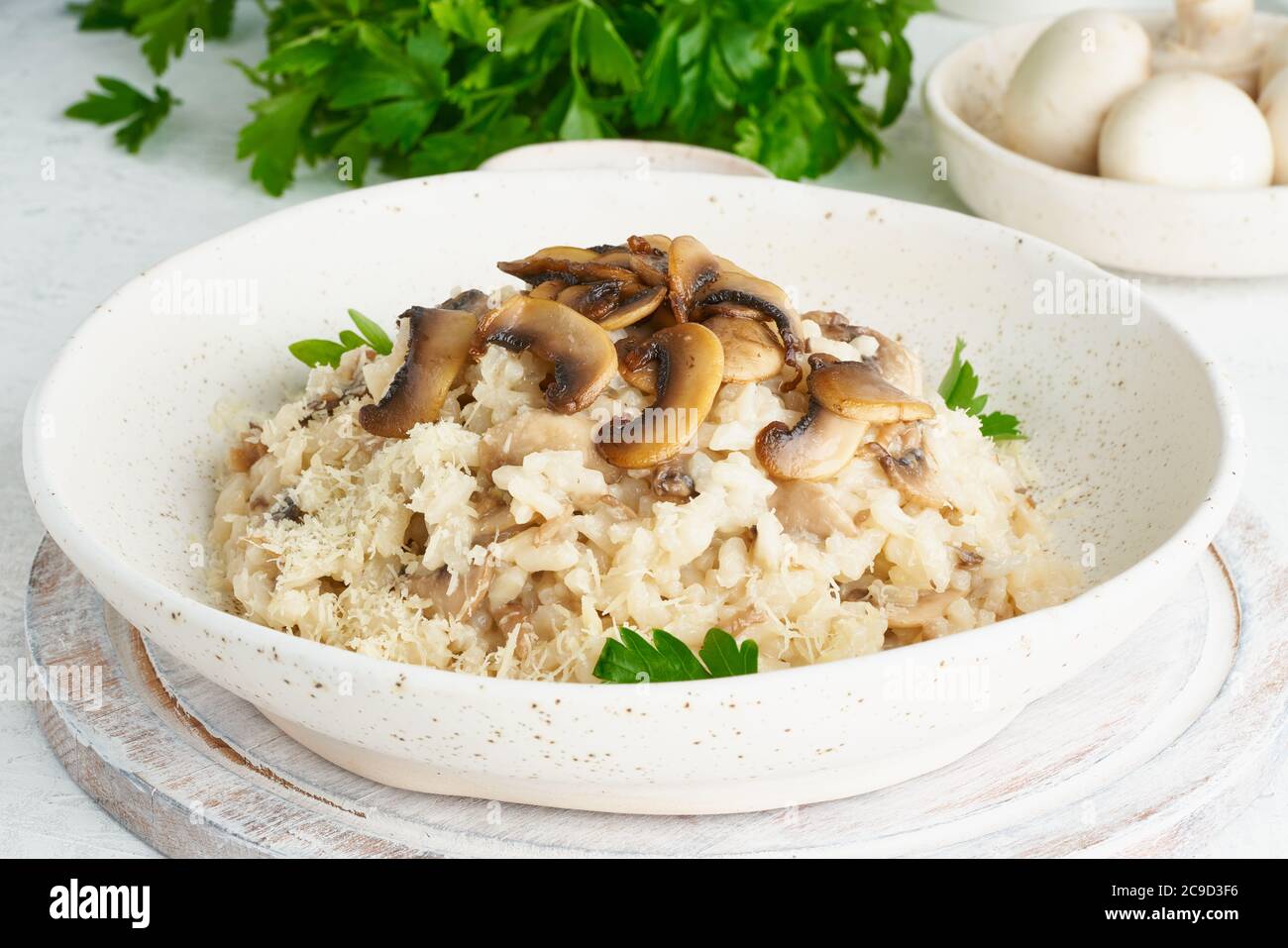 Risotto mit Pilzen in Teller. Reisbrei mit Pilzen und Petersilie. Weißer Tisch, Löffel, Pilze. Warmes Gericht, italienische Küche, Seitenblick Stockfoto