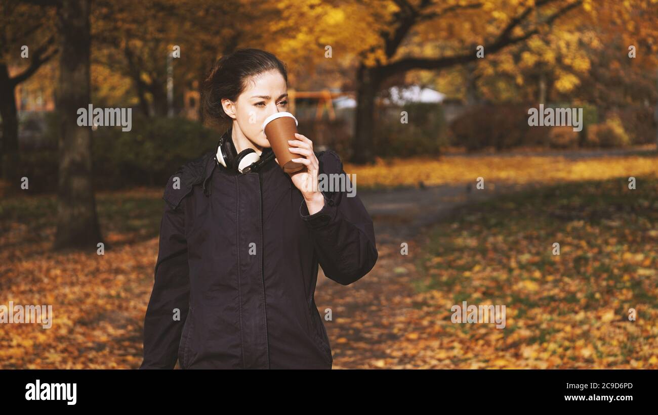 Junge Frau trinkt Kaffee aus Einweg-Tasse zu gehen, während zu Fuß im Park im Herbst Stockfoto