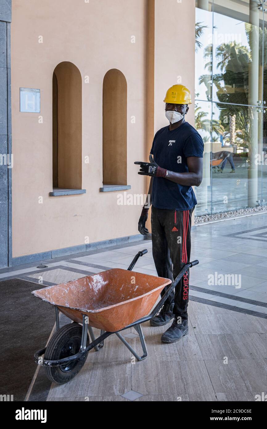 Bauarbeiter mit gelben Schutzmützen und Gesichtsmasken arbeiten an der Renovierung eines Hotels in Costa Adeje nach dem Covid 19 l Stockfoto