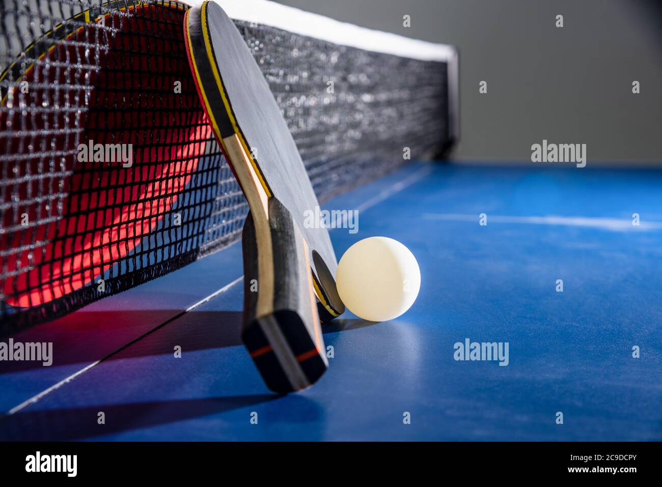 Closeup schwarz und rot Tischtennisschläger eine weiße Kugel auf der blauen Tischtennisplatte mit einem Netz, Tischtennis-Paddel ist eine Sportwettkampfausrüstung i Stockfoto