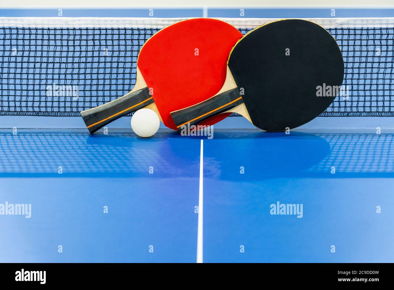 Schwarz und rot Tischtennisschläger und eine weiße Kugel auf der blauen Tischtennisplatte mit einem Netz, zwei Tischtennispaddel ist ein Sportwettkampfgerät i Stockfoto