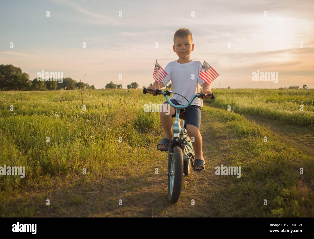 Junge auf dem Fahrrad in einem 4. Juli auf dem Wind auf dem grünen Feld. Patriotische Familie feiert Verfassung und Vatertag. Stockfoto