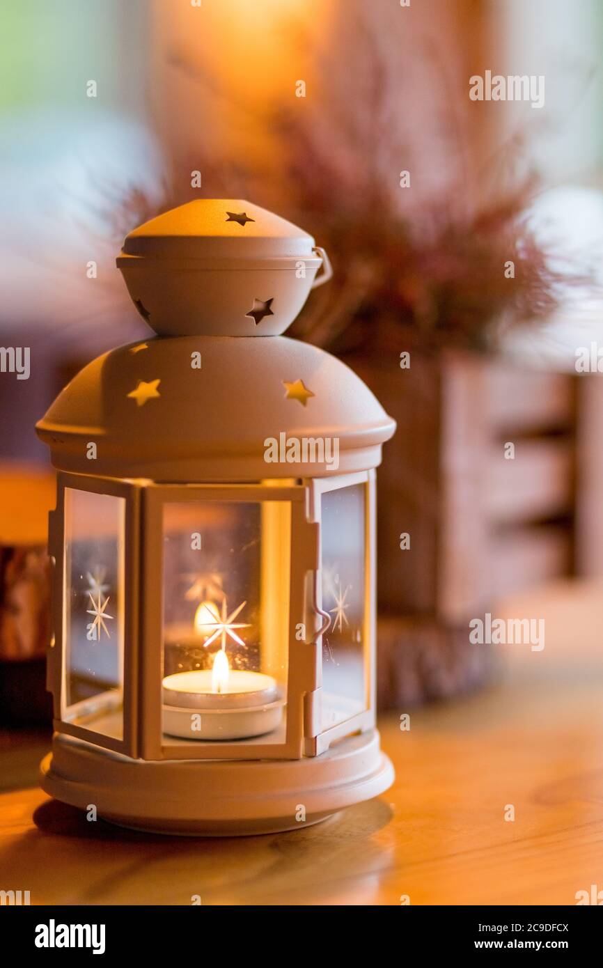 Schöne weiße Laterne mit brennender Kerze im Inneren auf Holztisch. Getöntes Bild. Romantische weiße Laterne. Weihnachtsschmuck Stockfoto