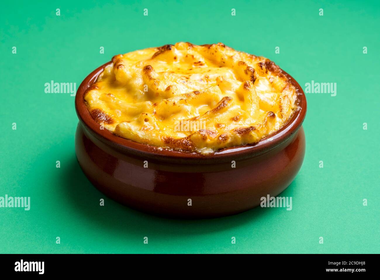 Käsemakkaroni in einer Keramikschale isoliert auf einem grünen Hintergrund. Gekochter mac und Käse mit weißer Sauce und Cheddar. Stockfoto