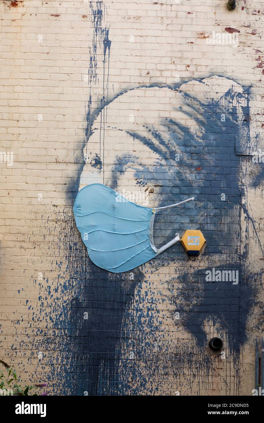„Mädchen mit einem durchbohrten Trommelfell“ mit zusätzlicher medizinischer Gesichtsmaske während der Pandemie von Covid 19. Banksy Graffiti-Künstler arbeiten am Hanover Place, in Br Stockfoto