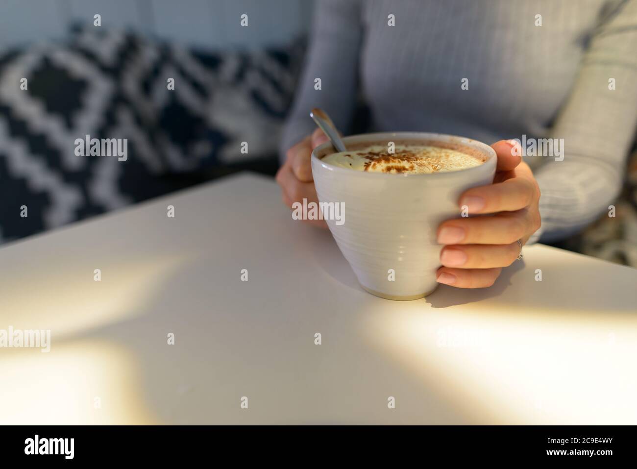 Fokussierte Aufnahme der jungen Frau hält köstliche Tasse Cappuccino mit Schaum und Schokolade bestreut Stockfoto