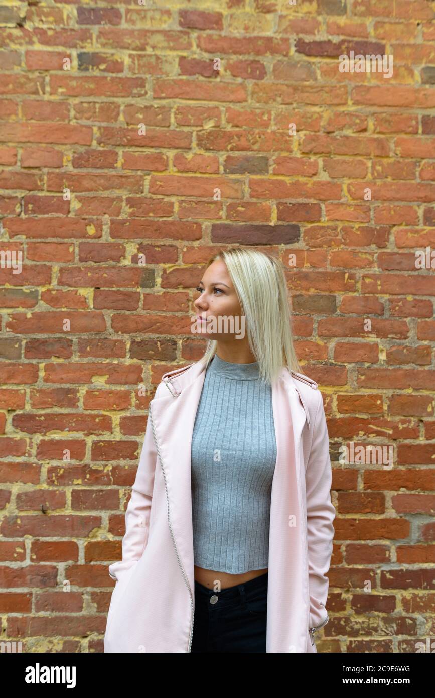 Junge schöne blonde Frau steht gegen Backsteinmauer Stockfoto