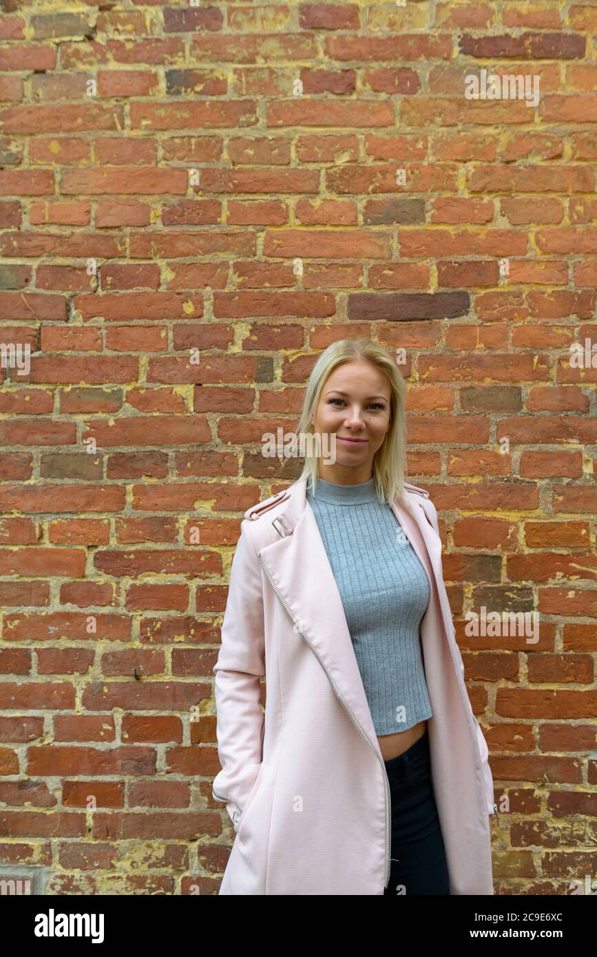 Junge schöne blonde Frau steht gegen Backsteinmauer Stockfoto