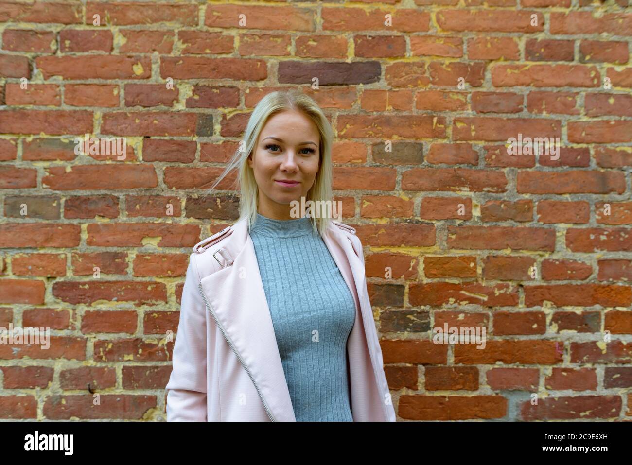 Junge schöne blonde Frau steht gegen Backsteinmauer Stockfoto