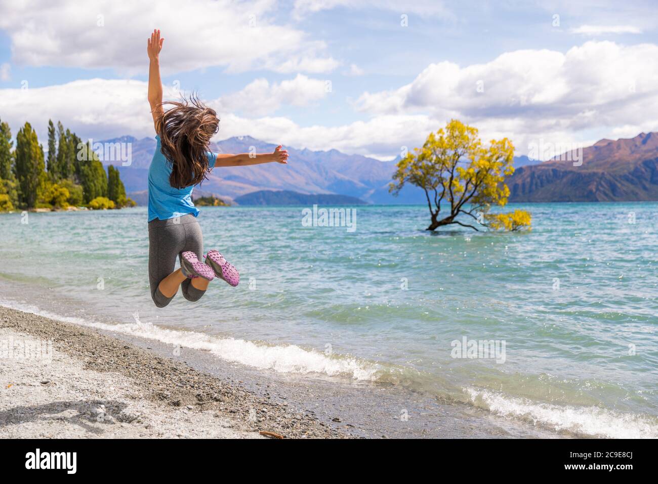 Neuseeland Reise glücklich Tourist Frau Springen der Freude an Wanaka Seenlandschaft mit eintem Baum, berühmte Attraktion. Stockfoto