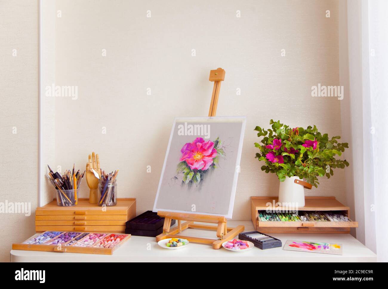 Auf dem Tisch steht eine hölzerne SkizzenStaffelei einer rosa Hagebuttenblume Stockfoto
