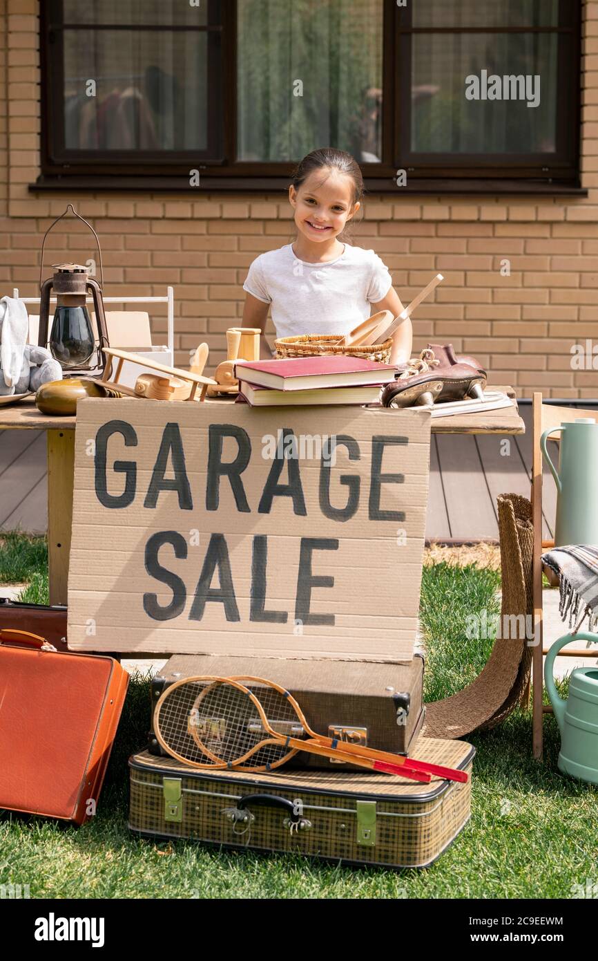 Portrait von lächelnd schönes Mädchen am Tisch stehen und bieten Dinge in der Garage Verkauf Stockfoto