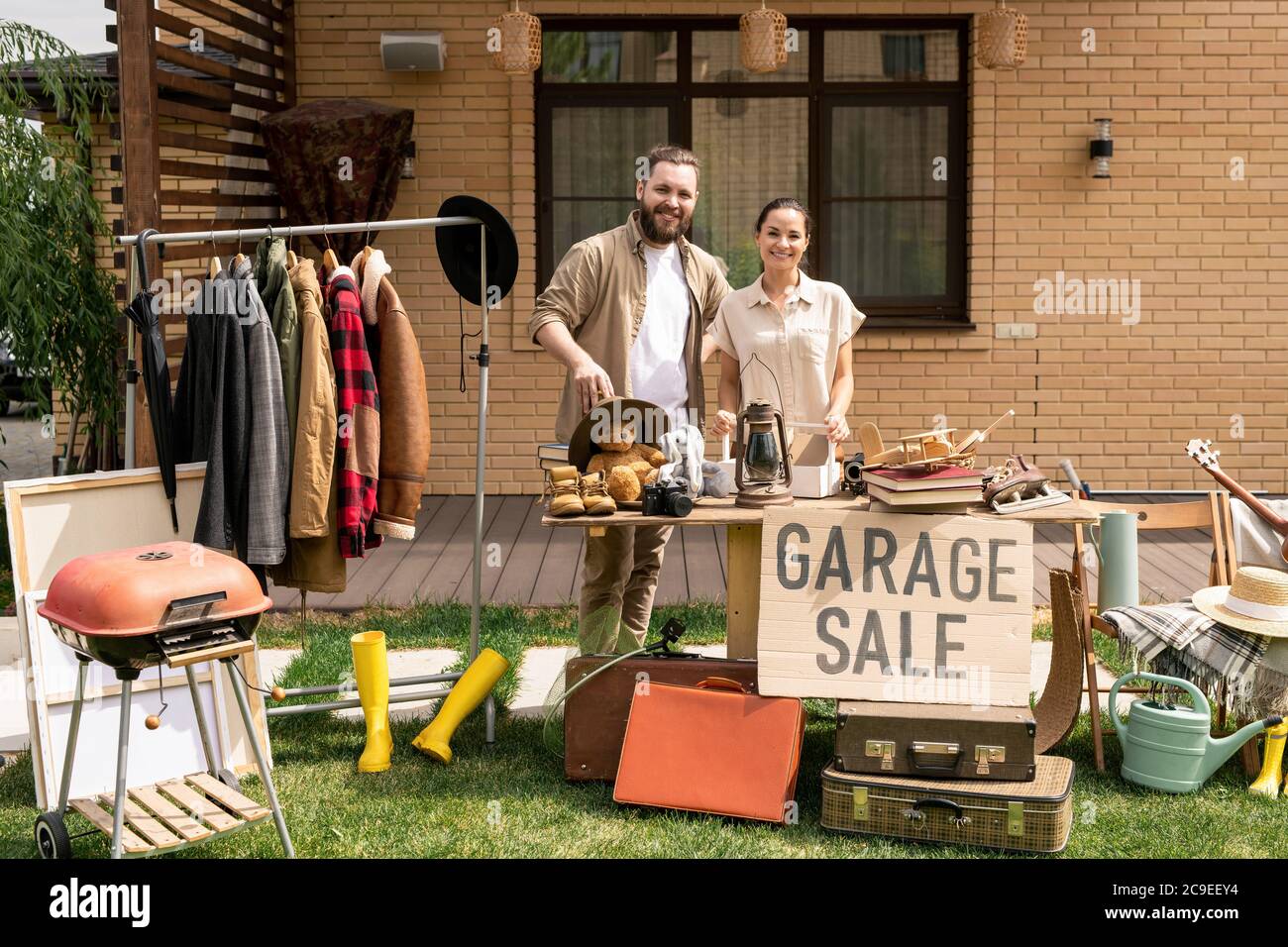 Portrait von fröhlichen jungen Paar Hosting Garage Verkauf im Hinterhof beim Verkauf nutzlose Sachen vor dem Umzug Stockfoto
