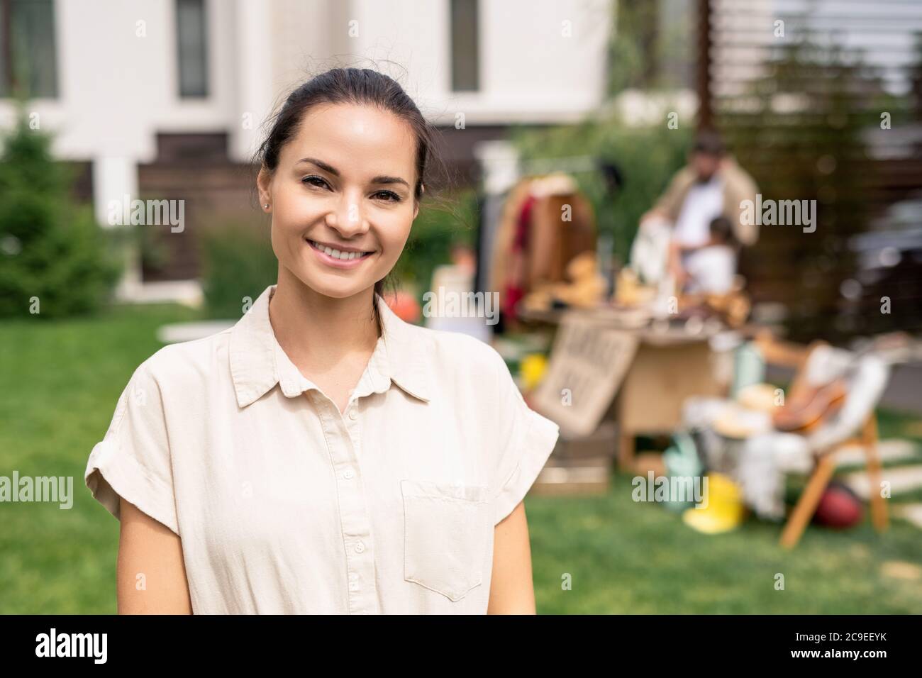 Portrait von lächelnd attraktive junge Frau in beige Bluse Besuch Garage Verkauf, um Waren für den Innenraum zu kaufen Stockfoto