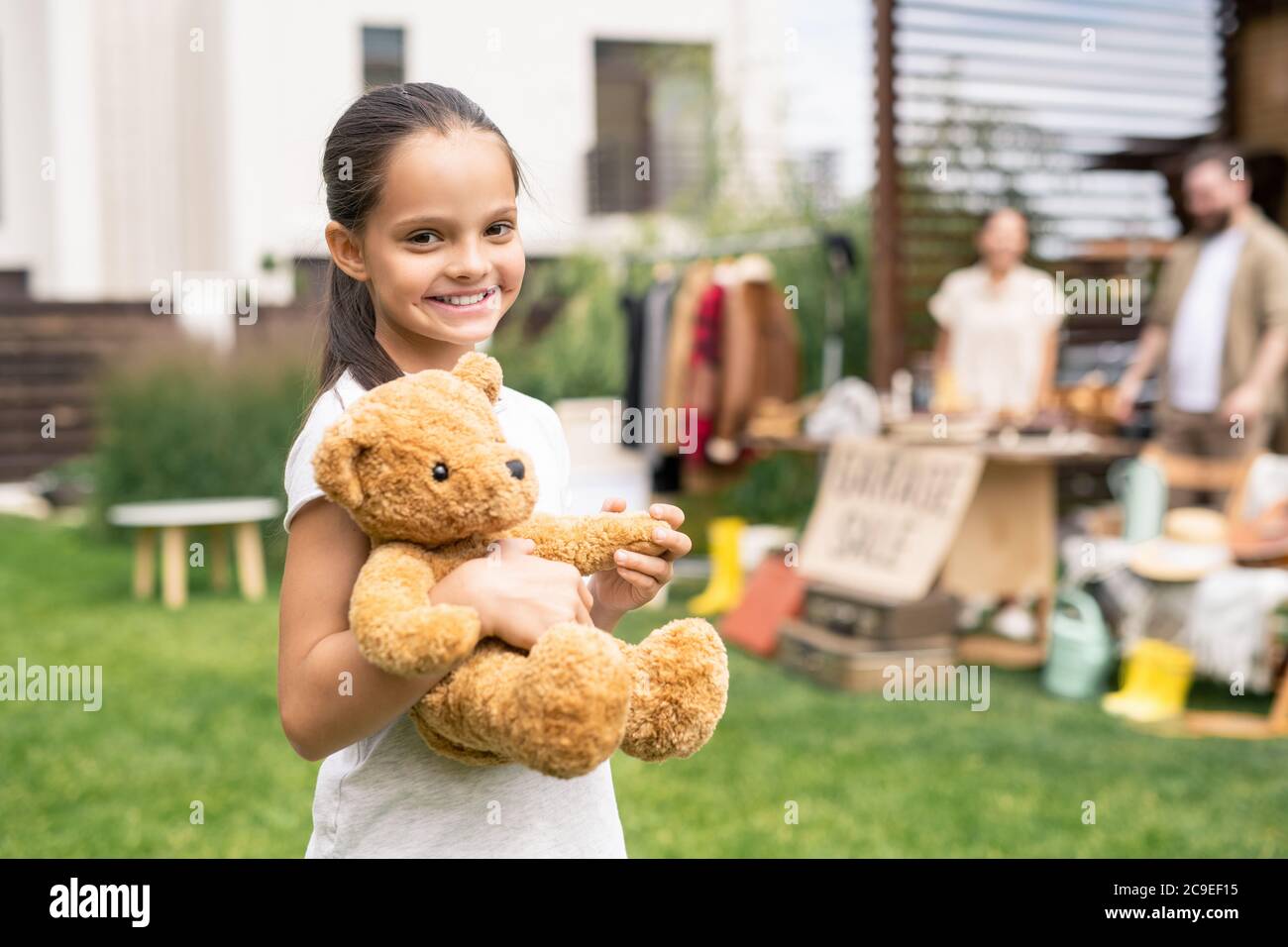 Portrait von lächelnd Brünette Mädchen hat Spielzeug in der Garage Verkauf stehen mit ihm im Hinterhof gefunden Stockfoto
