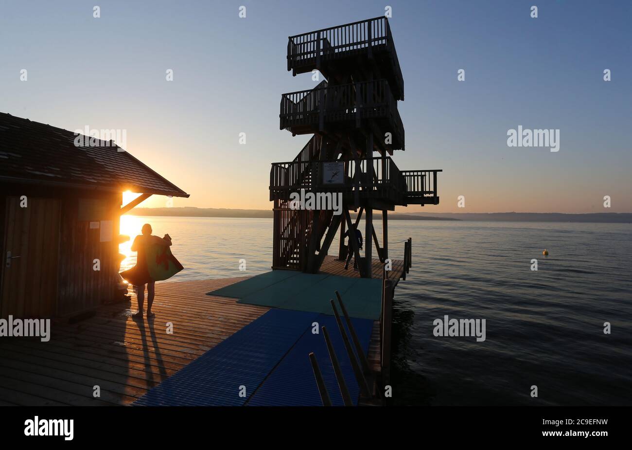 Utting, Deutschland. Juli 2020. Ein früher Badegast trocknet sich bei Sonnenaufgang auf dem Steg eines Strandbades mit einem Handtuch. Quelle: Karl-Josef Hildenbrand/dpa/Alamy Live News Stockfoto