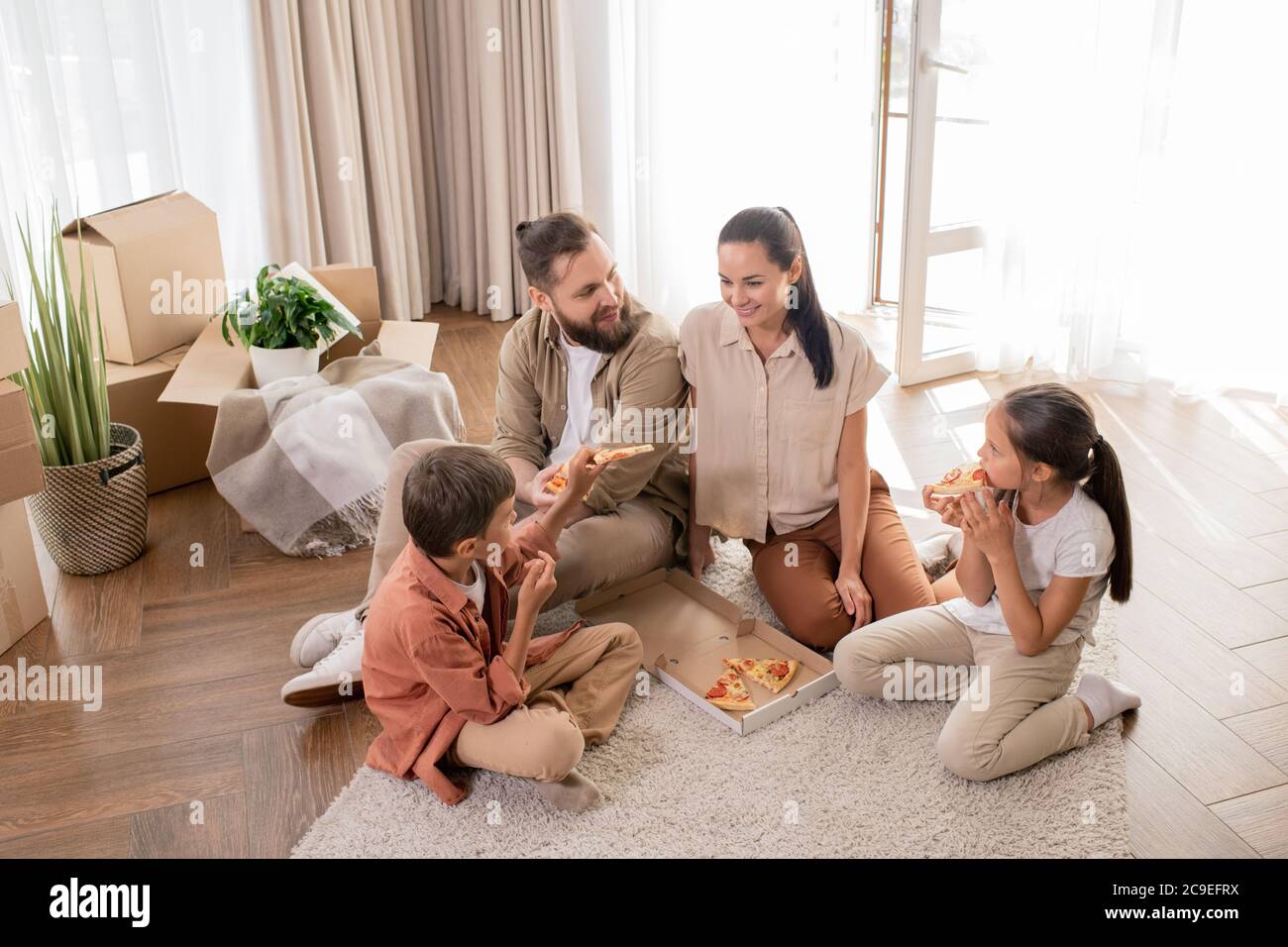Oben Blick auf glückliche junge Familie mit zwei Kindern auf dem Boden sitzen und genießen erstes Abendessen im neuen Haus Stockfoto