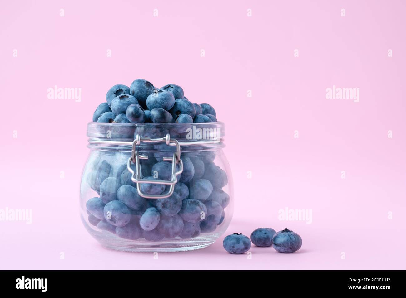 Heidelbeeren in einer Glasschale auf einem rosa Hintergrund, eine Beere in einem Glaskrug. Vegetarisches Konzept Stockfoto