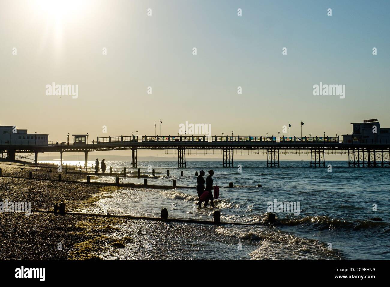 Worthing Beach, Worthing, Großbritannien. Juli 2020. Die Sonne geht über dem Pier und dem Beobachtungsrad auf, was vorausgesagt wird, einer der heißesten Tage des Jahres zu sein. Zwei offene Schwimmer betreten das Meer. Bild nach Kredit: Julie Edwards/Alamy Live Nachrichten Stockfoto