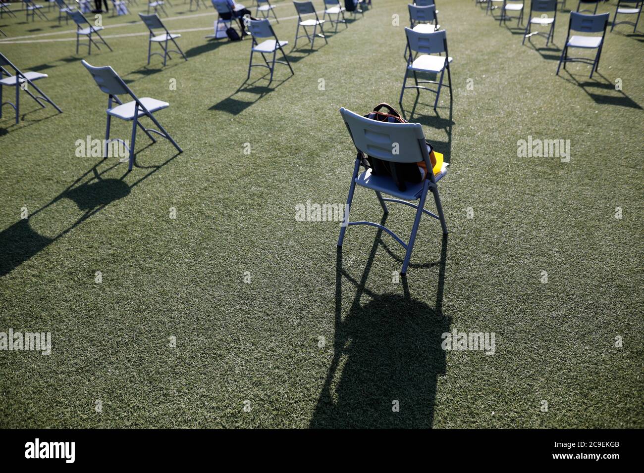 Stühle auseinander, um die soziale Distanz während der Covid-19 Ausbruch bei einem Outdoor-Event auf dem Rasen eines Stadions zu halten. Stockfoto