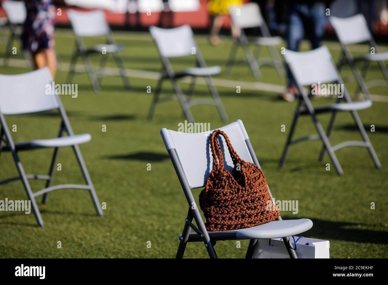Stühle auseinander, um die soziale Distanz während der Covid-19 Ausbruch bei einem Outdoor-Event auf dem Rasen eines Stadions zu halten. Stockfoto