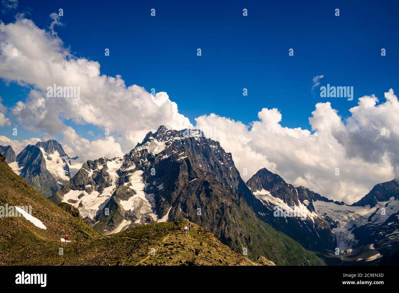 Schneebedeckter Berg gegen bewölkten Himmel. Von unten schwimmen weiße Wolken am blauen Himmel über dem schneebedeckten Bergrücken an sonnigen Tagen in der Natur Stockfoto