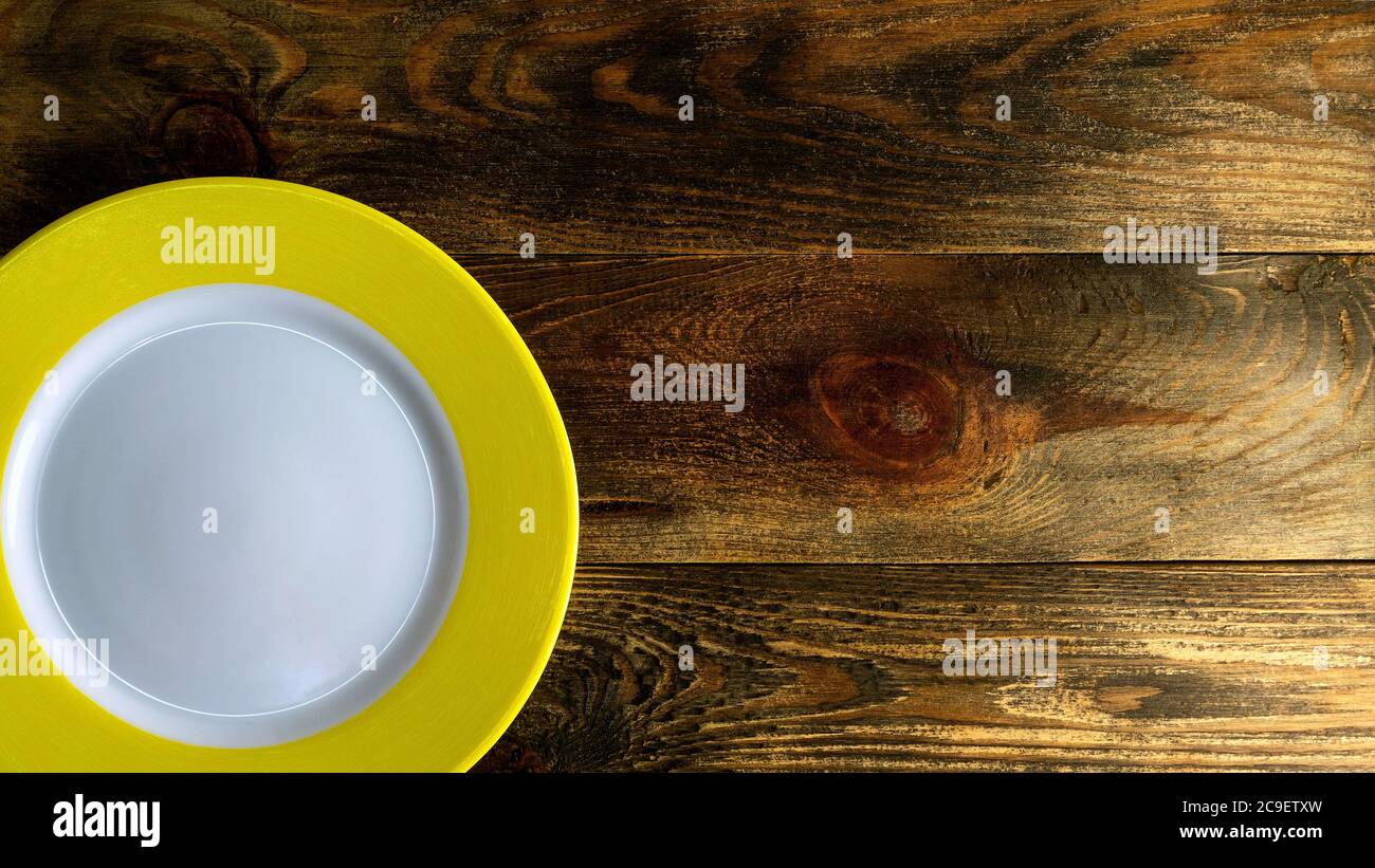 Leere runde Keramikplatte mit gelber Kante auf rauem Holzhintergrund oder Tisch. Platz für Text kopieren. Von oben nach unten. Flach liegend. 16x9-Format. Nahaufnahme. Innen Stockfoto