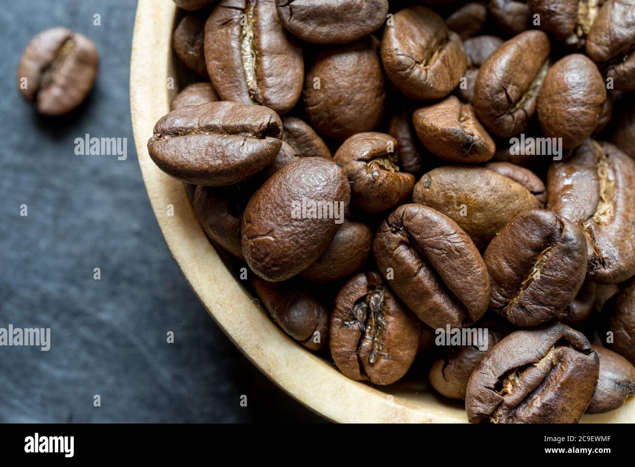 Extreme Nahaufnahme einer Holzschale gefüllt mit gerösteten Kaffeebohne auf dunklem Schieferhintergrund. Horizontales Format mit Platz für Text Stockfoto