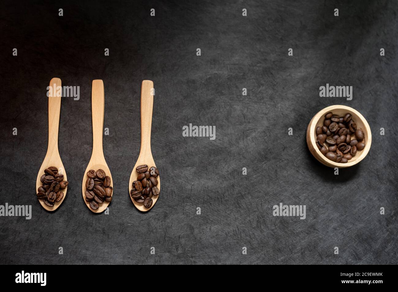 Draufsicht auf Holzlöffel und Schüssel gefüllt mit gerösteten Kaffeebohne auf einem dunklen Schieferhintergrund. Horizontales Format mit Platz für Text Stockfoto