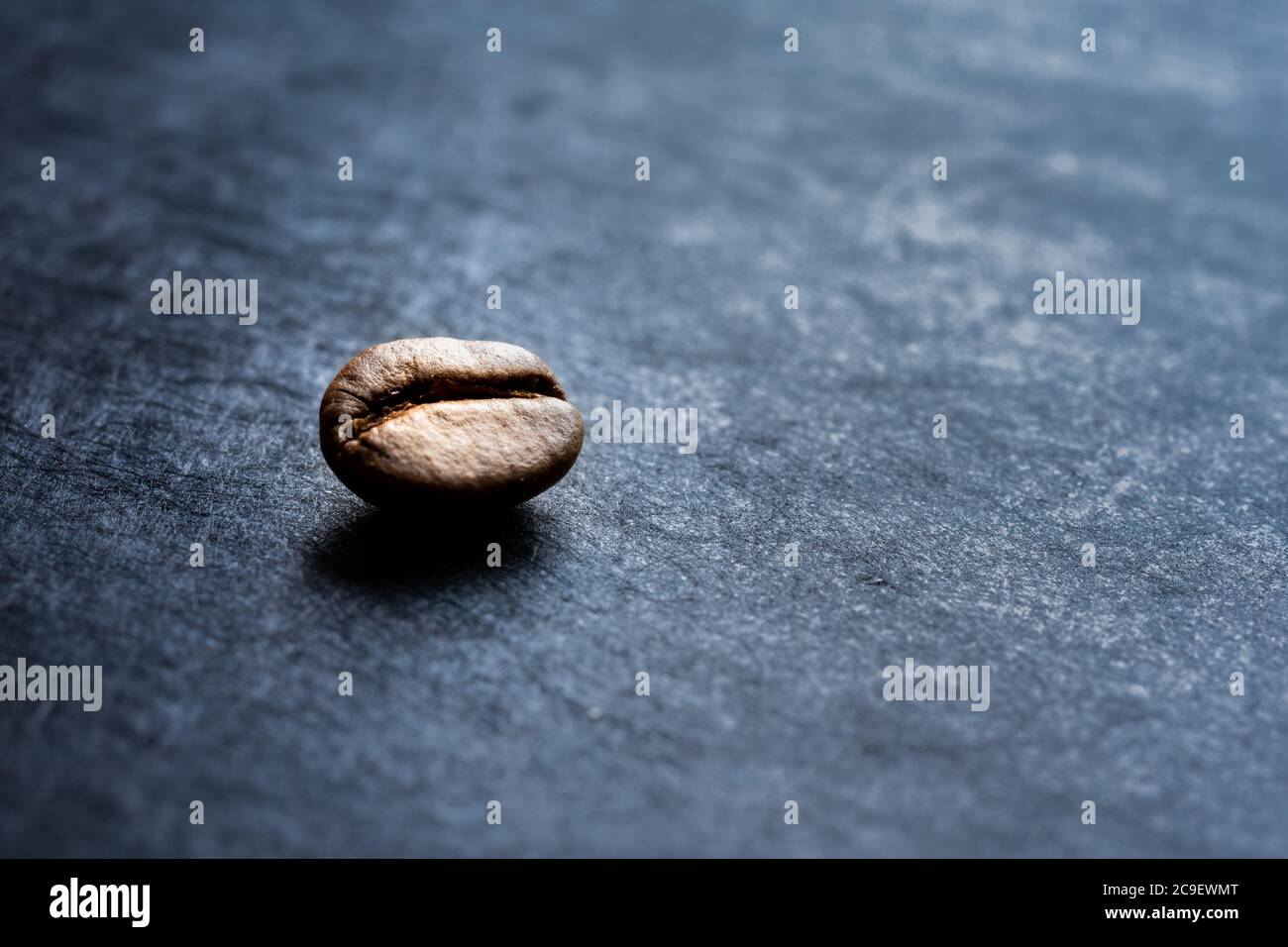 Nahaufnahme einer isolierten gerösteten Kaffeebohne auf dunklem Schieferhintergrund. Hochformat mit Platz für Text Stockfoto