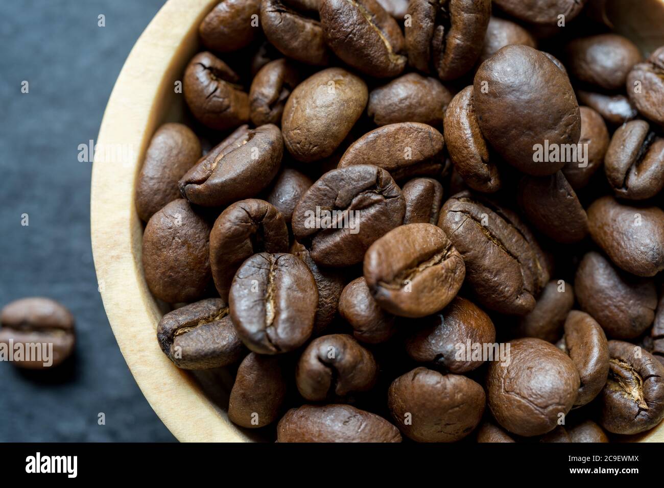 Extreme Nahaufnahme einer Holzschale gefüllt mit gerösteten Kaffeebohne auf dunklem Schieferhintergrund. Horizontales Format mit Platz für Text Stockfoto
