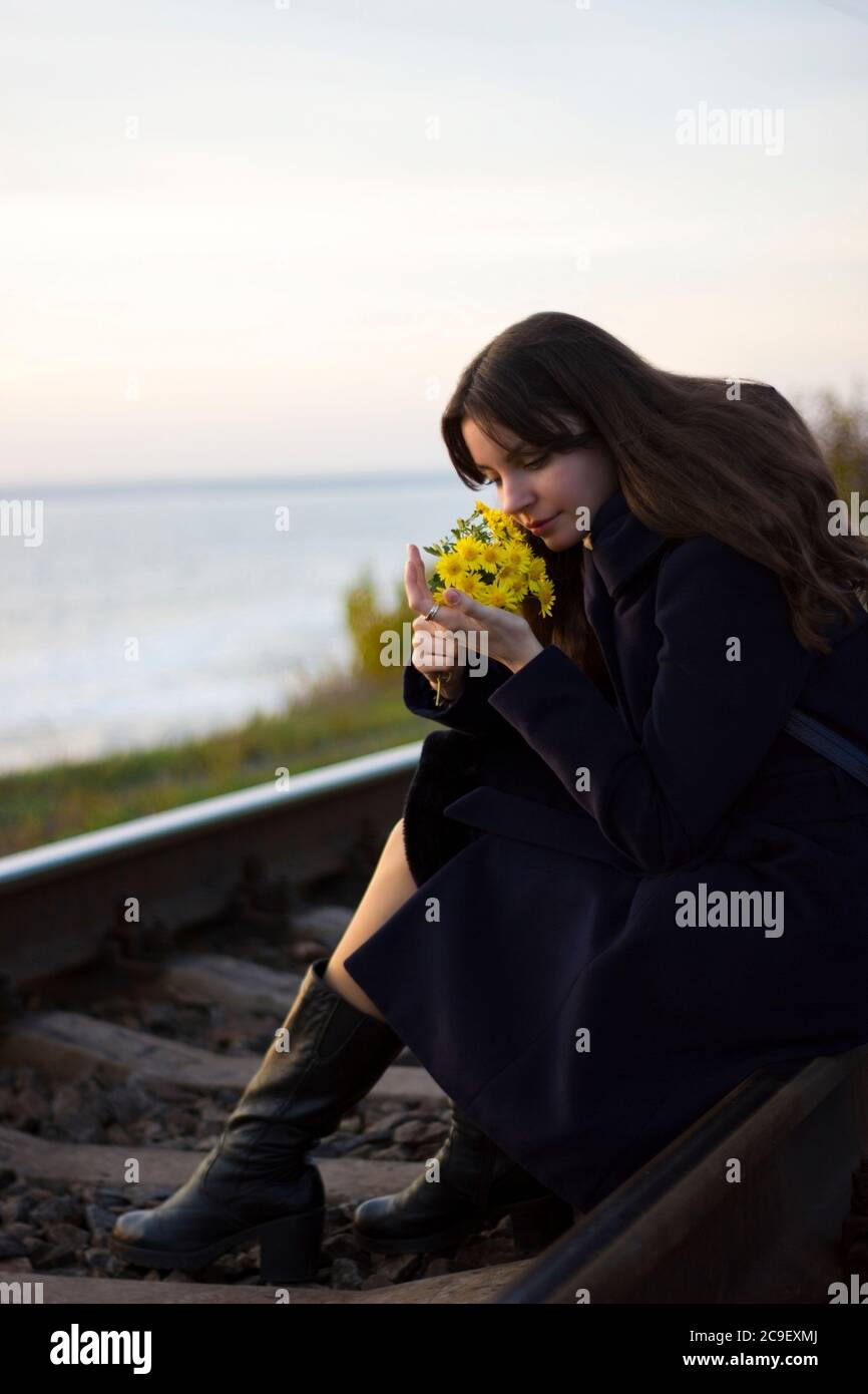 Mädchen geht auf Eisenbahnschienen in einem Mantel mit Blumen - Reisen, Depression, Lifestyle, Liebe Stockfoto