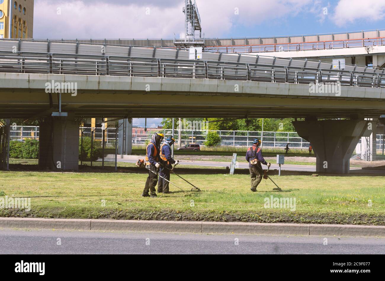 Sankt Petersburg, Russland - 26. Juli 2020: Drei Arbeiter in Overalls mähen das Gras auf dem Rasen mit Trimmern Stockfoto
