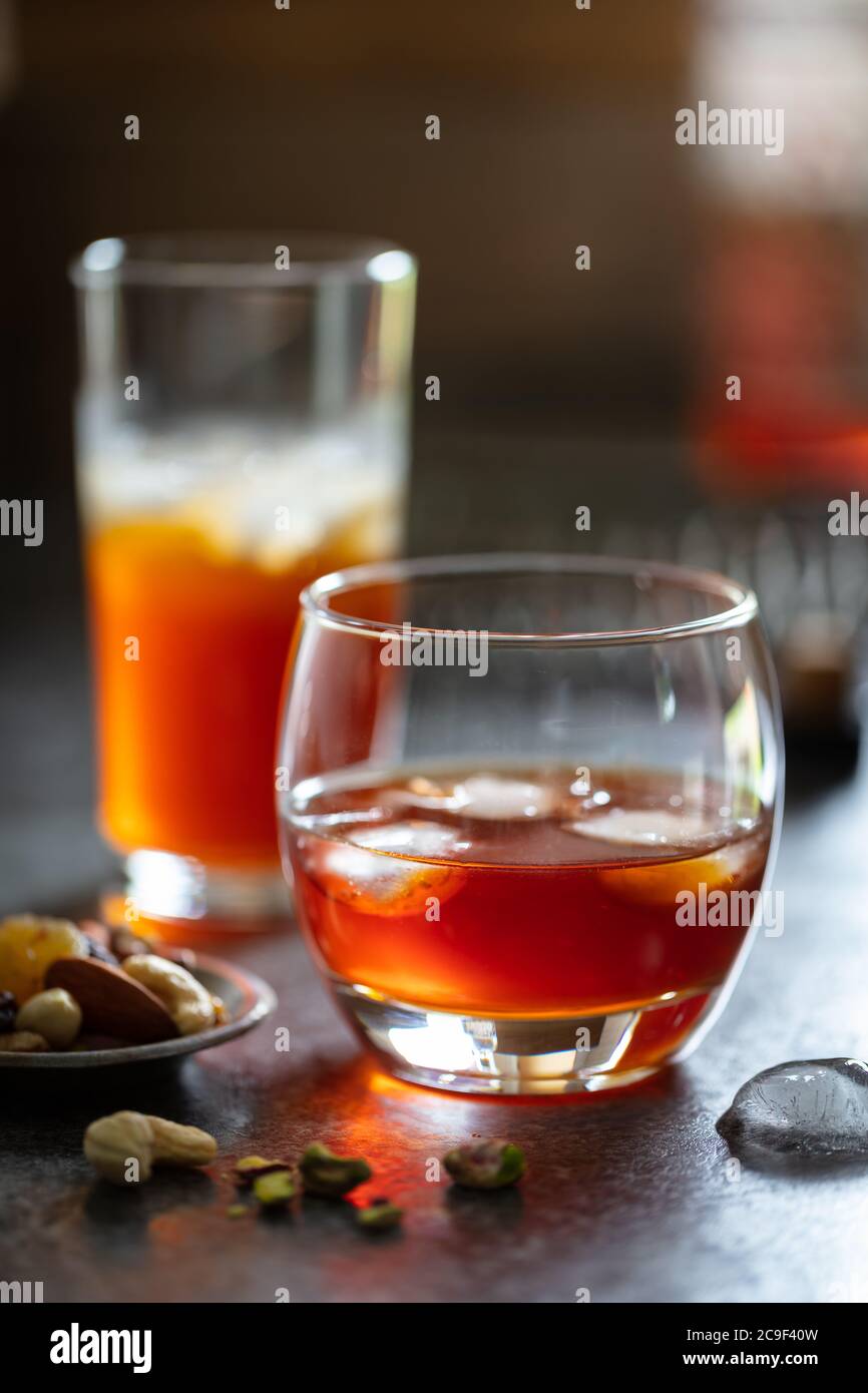 Alkoholische Getränke (Whiskey Wermouth) mit Eis auf dunkler Arbeitsplatte. Gericht mit Knabbereien. Hochformat Stockfoto