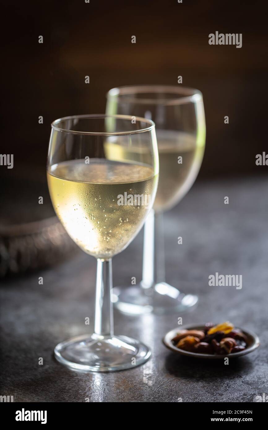 Gekühlter Weißwein mit Knabbereien auf dunklem Hintergrund. Diners-Perspektive. Hochformat. Stockfoto