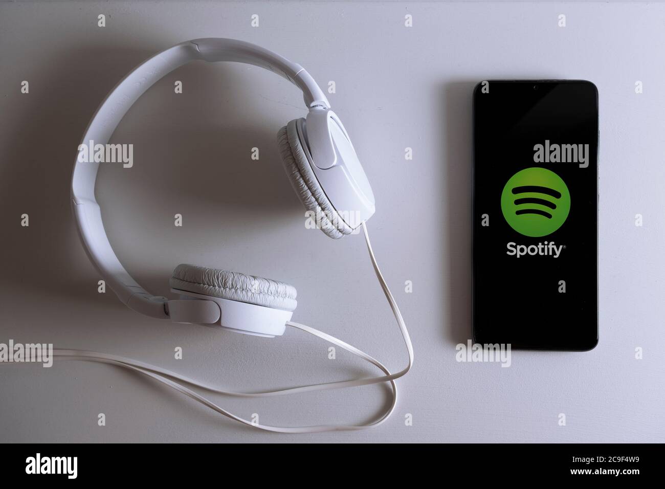 Spotify App-Logo auf einem Smartphone-Bildschirm, auf dem die Anwendung ausgeführt wird. Streaming-Musikdienst auf einem mobilen, nächsten, weißen Kopfhörer. Stockfoto