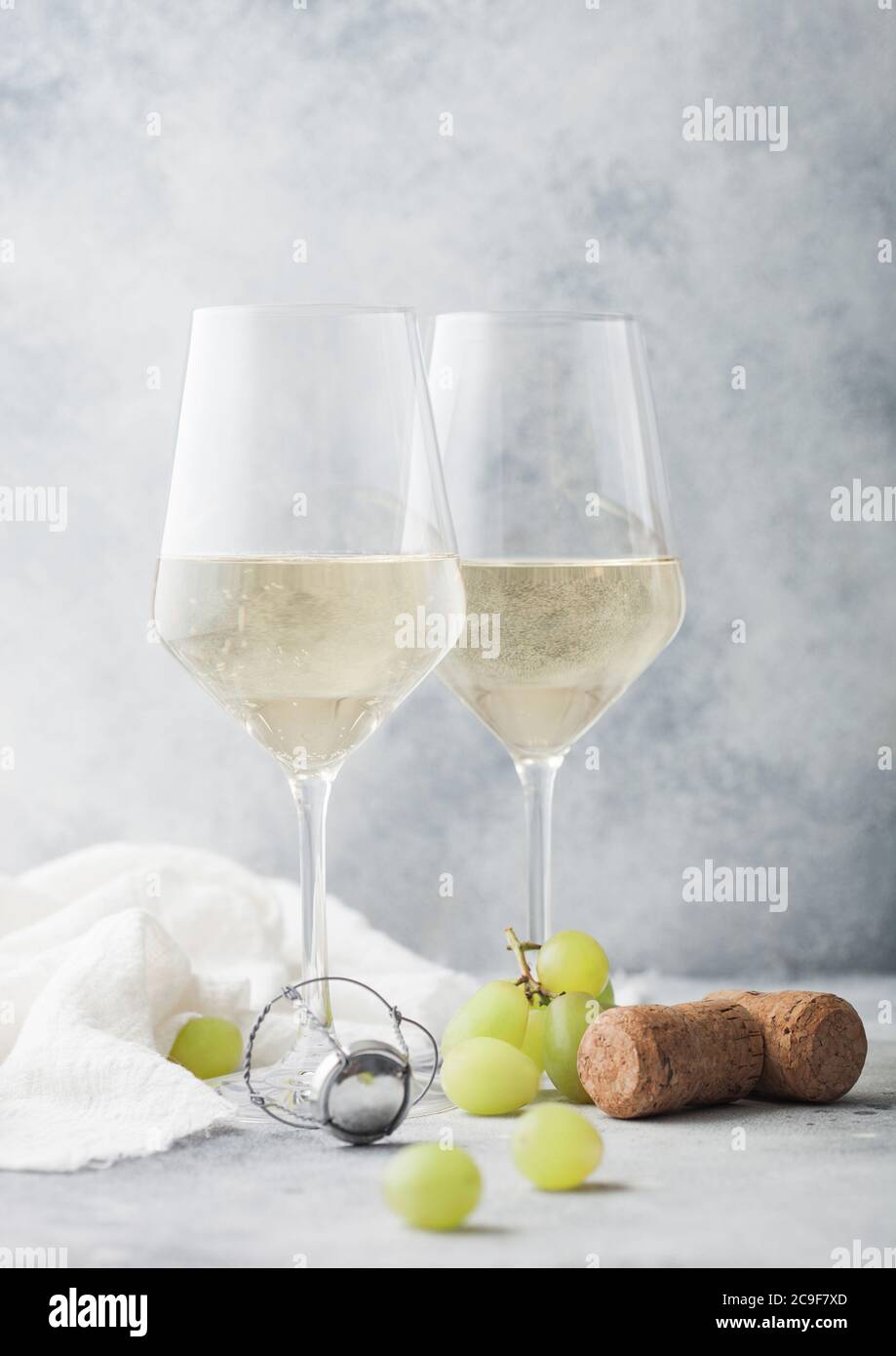 Zwei Kristallgläser aus weißem hausgemachten Wein mit Korken und Trauben auf hellem Tischhintergrund. Stockfoto