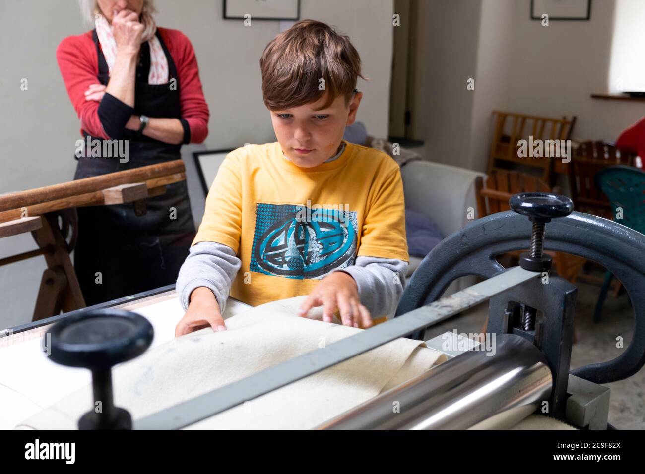 Junge lernen, eine Littlejohn-Radierpresse zu benutzen, während sie Grafikkunst in einem Workshop-Studio in Carmarthenshire Wales UK LERNEN KATHY DEWITT Stockfoto