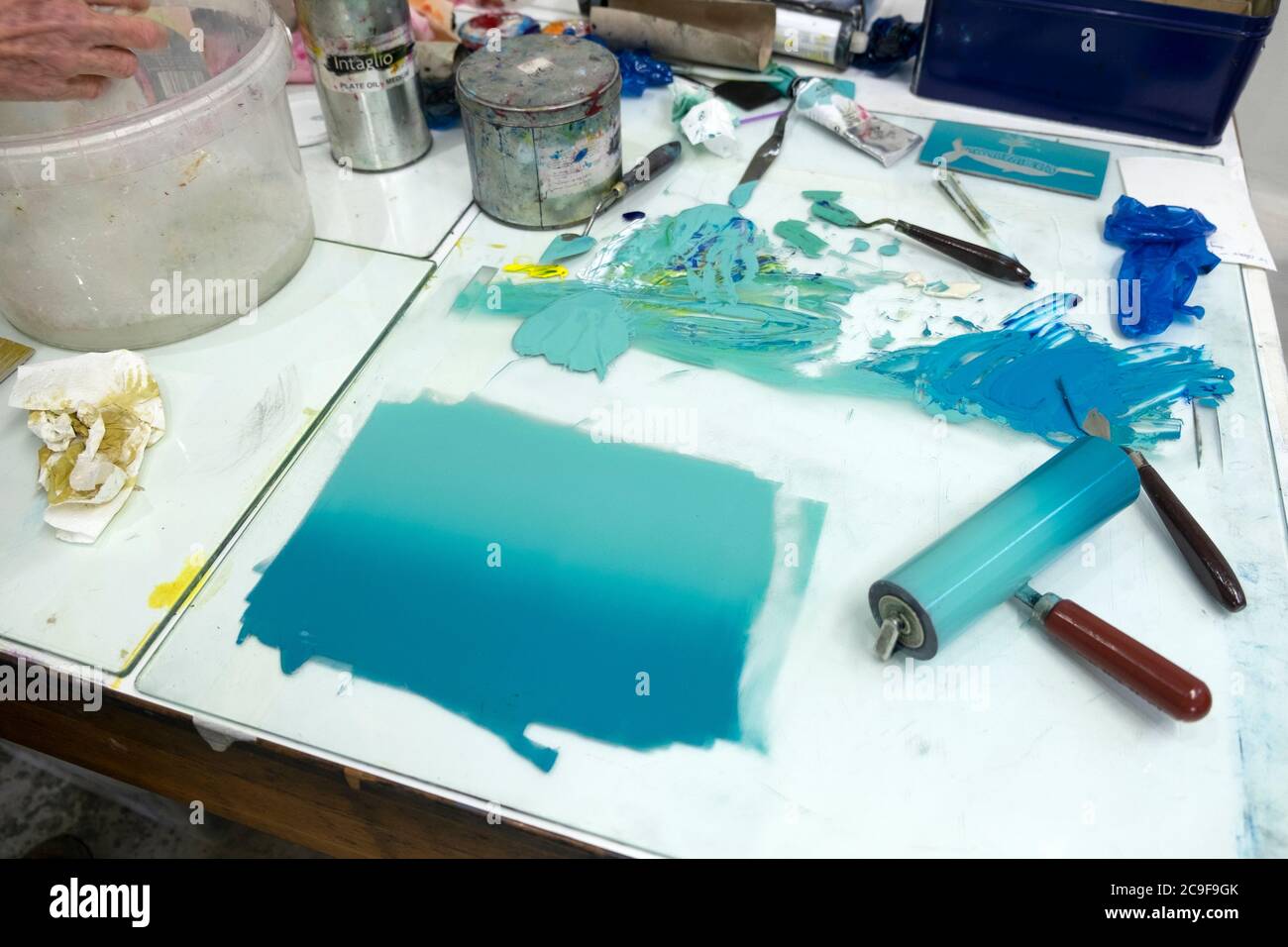 Türkisblaue Tinte auf einem Glasoberfläche Tisch mit Walze und Werkzeuge für die Herstellung von Lino Cut Prints in Grafik-Werkstatt Wales UK KATHY DEWITT Stockfoto