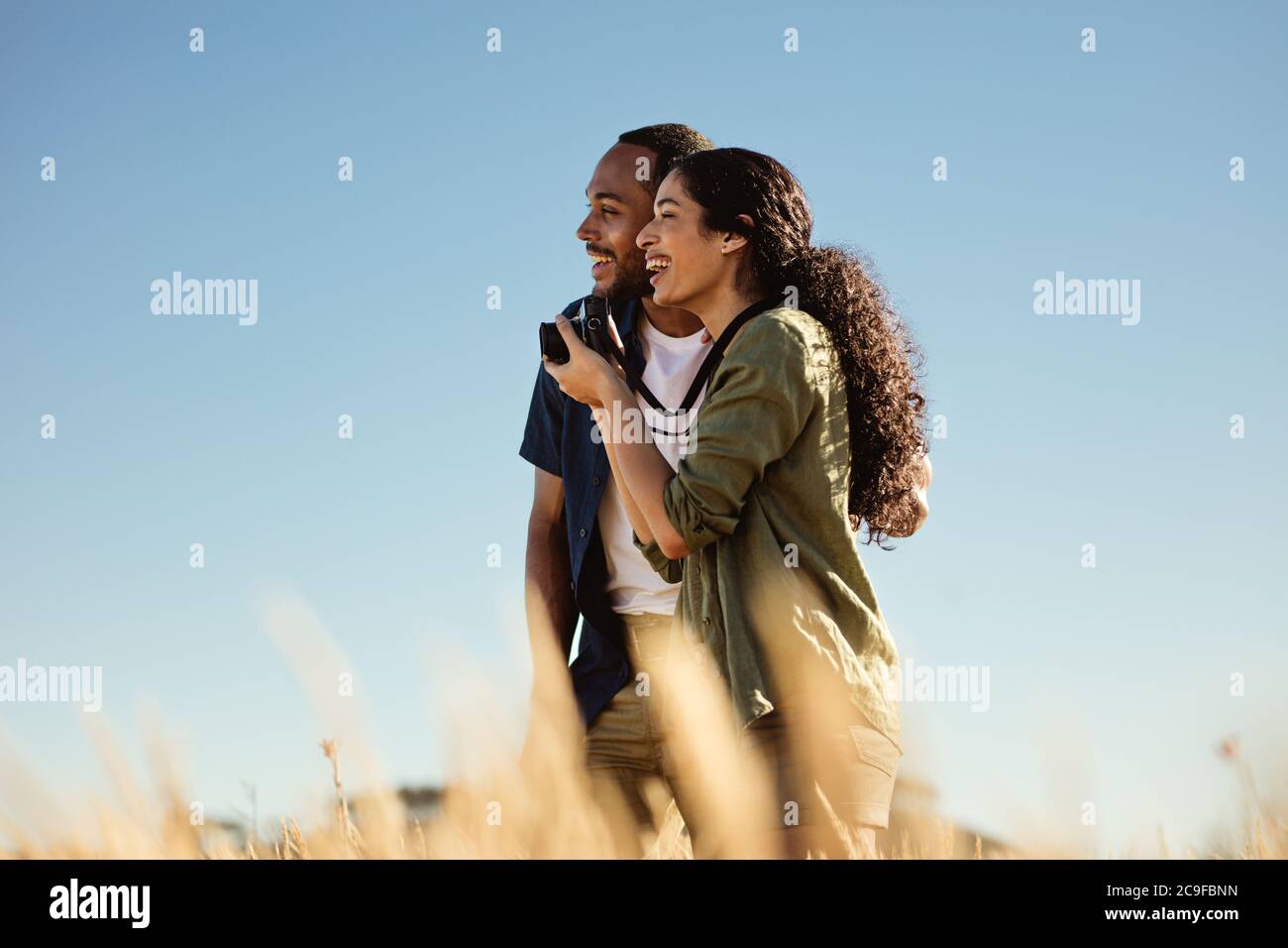 Porträt eines lächelnden Touristen-Paares, das auf dem Feld zusammensteht und wegschaut. Glückliches Paar genießen enge Momente in einem Urlaub. Stockfoto