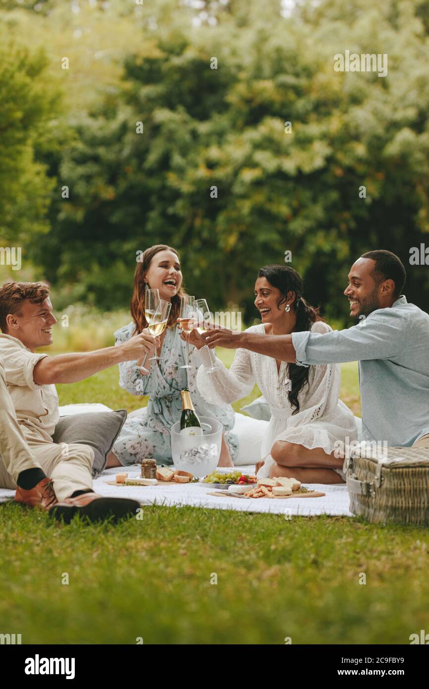 Fröhliche Freunde toasten im Park. Junge Leute toasten Champagner, während sie im Park sitzen. Stockfoto