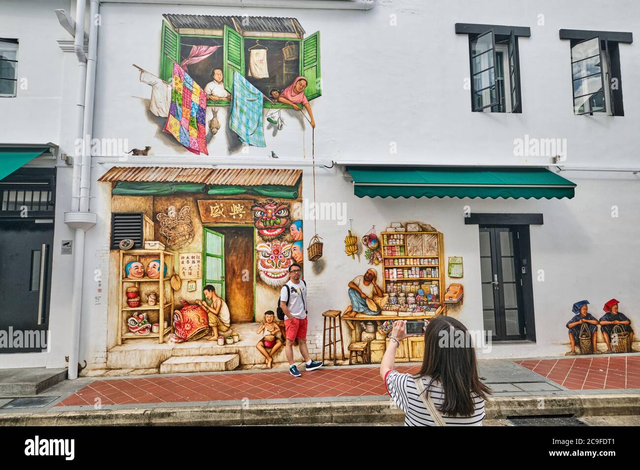 Ein touristisches Paar, das vor einem umfangreichen Wandgemälde des Künstlers Yip Yew Chong fotografiert; Mohamed Ali Lane, Chinatown, Singapur Stockfoto