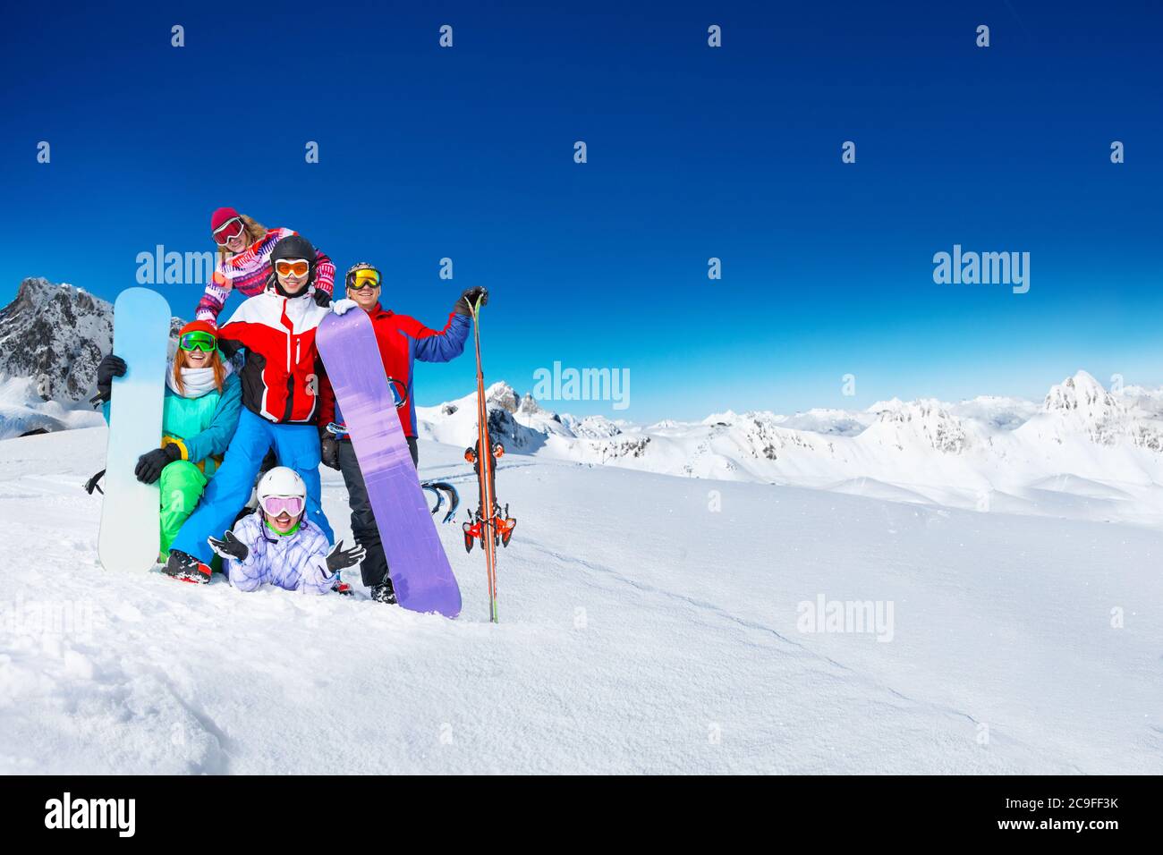 Gruppe junger Erwachsener Snowboarder posieren gemeinsam auf dem Gipfel des Berges über schneebedeckten Gipfeln bei sonnigem Wetter auf dem Rücken Stockfoto