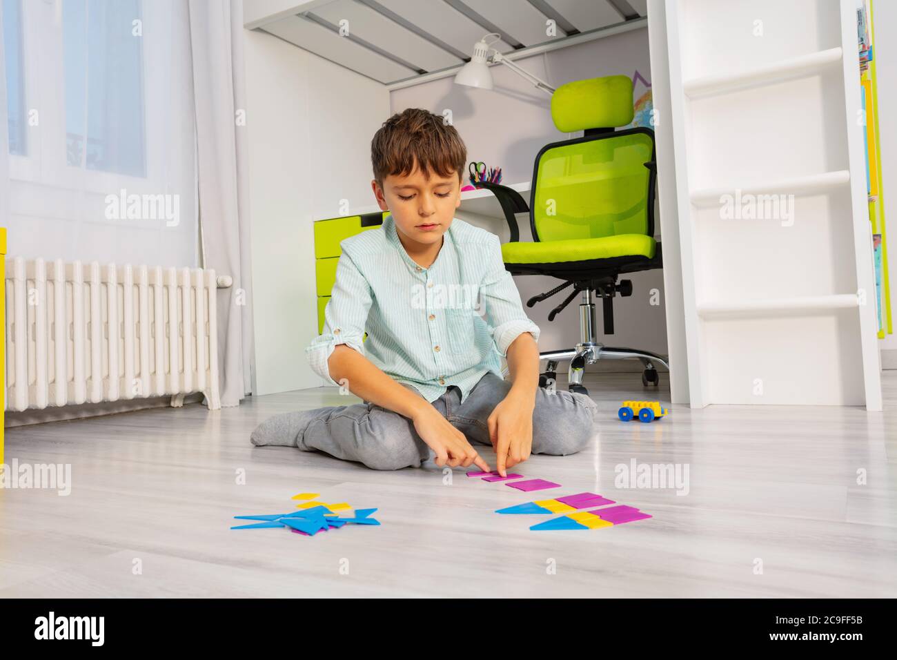Calm Junge legte geometrische Formen in Ordnung sitzen auf dem Boden im Kinderzimmer Stockfoto