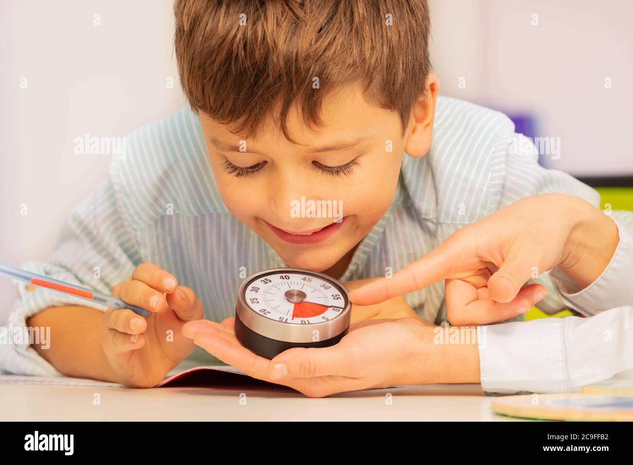 Junge mit Autismus-Spektrum-Störung während der ABA-Therapie Blick auf Lektion Timer in den Händen Lehrer Verständnis Zeit Konzept Stockfoto