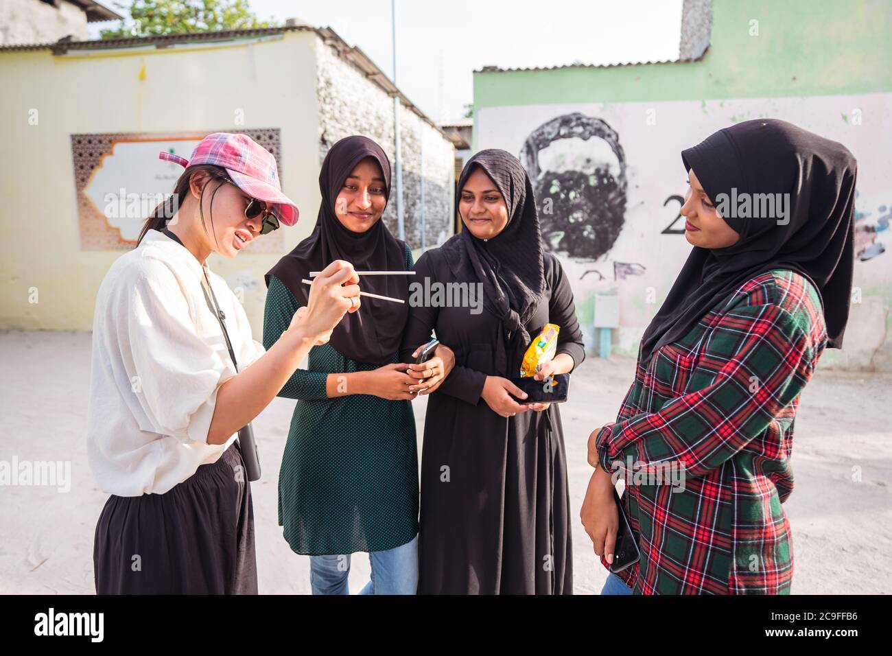 Bodufolhudhoo / Malediven - 17. August 2019: Junge Asiatin im Gespräch mit drei muslimischen einheimischen jungen Frauen mit schwarzem Hijab Stockfoto
