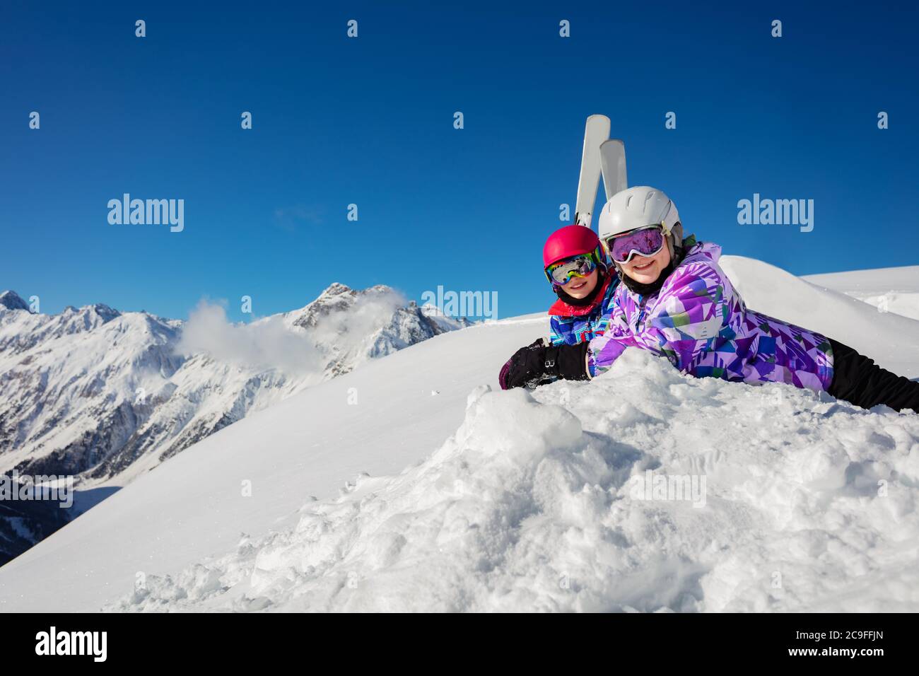 Zwei Mädchen lagen im Schnee über blauem Himmel und hohen Bergen mit Ski im Hintergrund Stockfoto