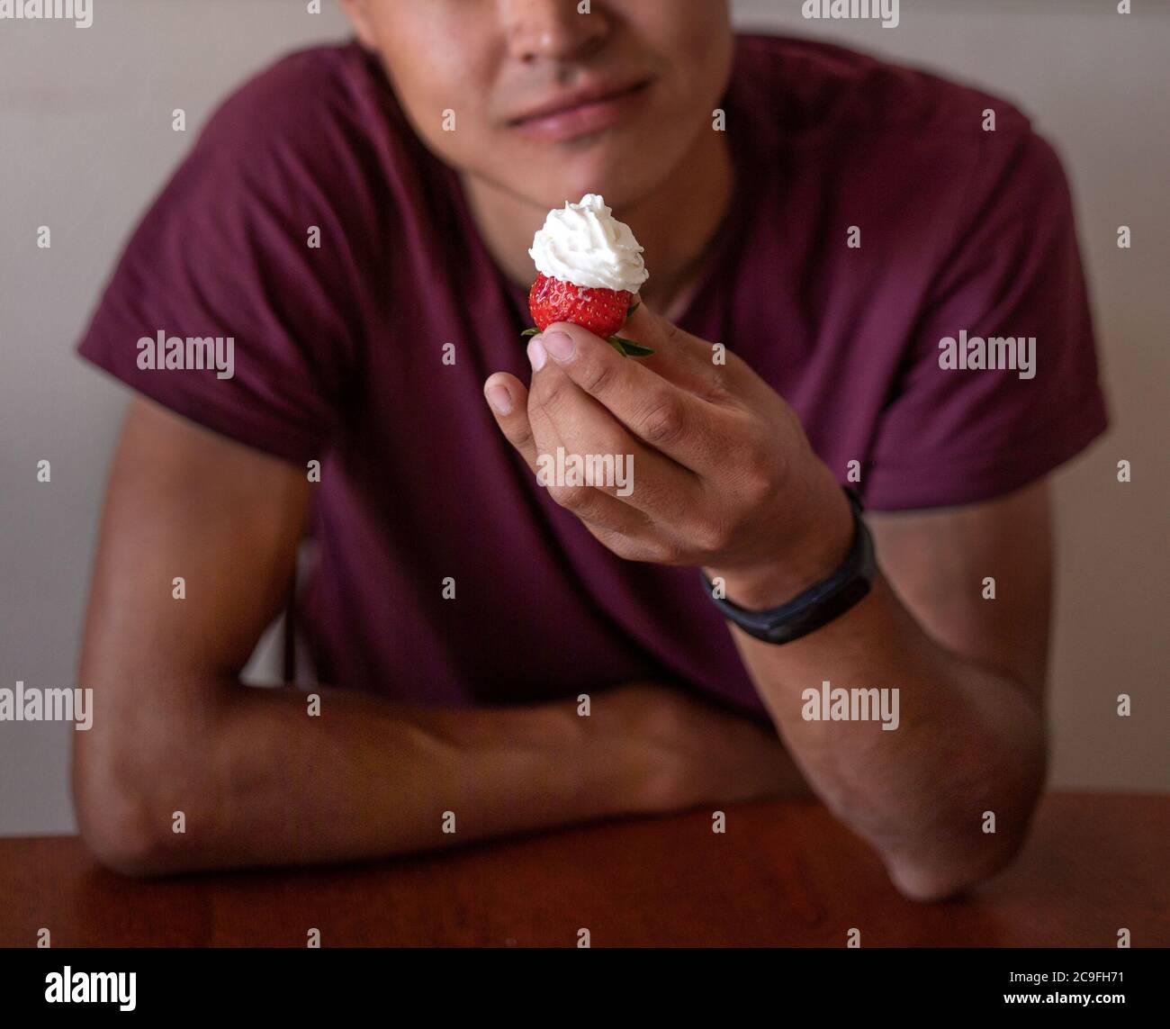 Guy sitzt am Tisch und hält Erdbeere mit Sahne in der Hand. Leckeres Essen, Dessert Stockfoto
